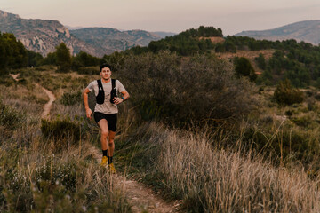 Endurance athlete running along a scenic mountain trail surrounded by vegetation during golden hour light. Concept of outdoor fitness, adventure running and healthy lifestyle.