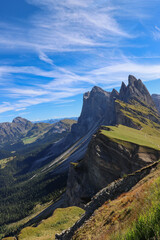 Panoramic view of Seceda ridge in the Dolomites, South Tyrol, Italy, showing dramatic jagged cliffs and lush alpine meadows under a clear summer sky