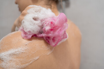 Fototapeta premium Close up of woman back washing with sponge and shower gel foam. Female scrubbing skin in bathroom. hygiene, body care, skincare and wellness routine in shower.