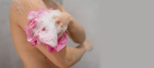 Beautiful young woman washing body with sponge and shower gel. Female lathering skin with soap foam...