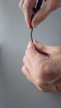 Closeup hands testing damaged cable end, DIY homeowner assessing charger connector bend and sheath wear on gray table, visual continuity check and practical troubleshooting, mobile