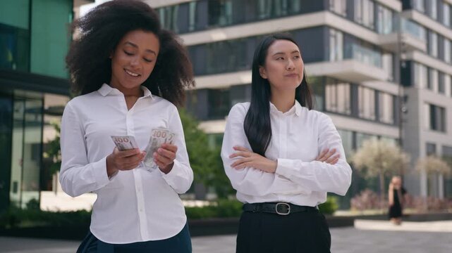 Jealous Asian Korean worker African American business women looking at money in city outdoors envious cash counting banknotes discrimination businesswomen salary injustice financial girls females work