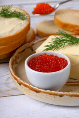 Red caviar in a white bowl, butter, wheat bread and a sprig of dill on a ceramic plate on a white table. Ingredients for a sandwich. Close-up. Superfood, healthy eating