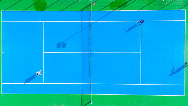 Aerial view of vibrant turquoise tennis court where shadows stretch long as players duel under the sun, Novi Sad, Vojvodina, Serbia.
