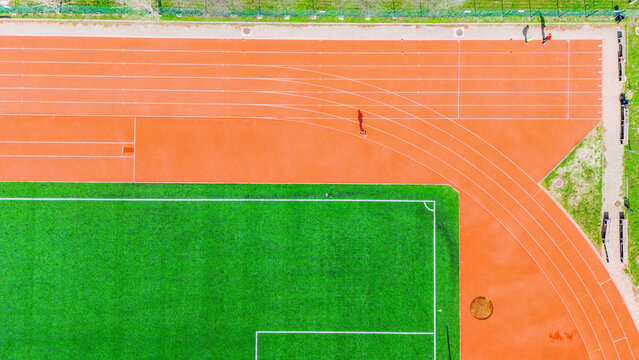 Aerial view of the vibrant orange track meeting the lush green field in a stunning contrast of color and form, Novi Sad, Vojvodina, Serbia.