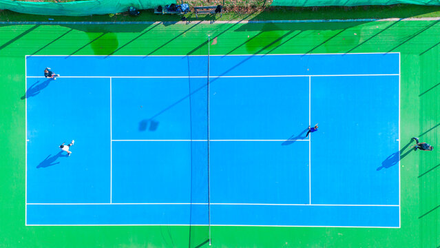 Aerial view of a tennis court bathed in bright blue, contrasting with the vibrant green surroundings, Novi Sad, Vojvodina, Serbia.