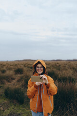 Young woman lifestyle outdoors wearing orange jacket and glasses takes photo with smartphone in...