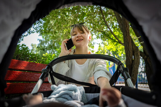 A cheerful nanny playing with a baby in a stroller while talking on the phone garden.