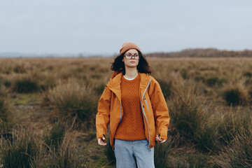 Woman lifestyle outdoors in autumn field wears orange jacket and knitted hat, walking confidently...