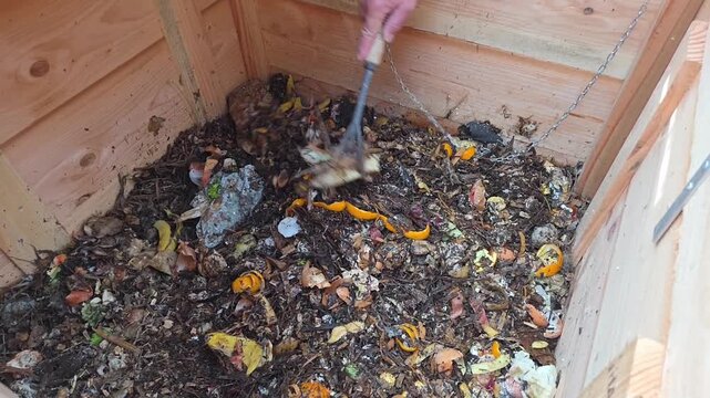Main qui m&eacute;lange le compost avec la mati&egrave;re brune dans le bas de compost du jardin