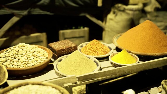 Colorful spice cones on wooden stall, warm yellow light highlights textures of turmeric, pulses and mixed grains in shallow bowls, intimate closeup evokes aroma