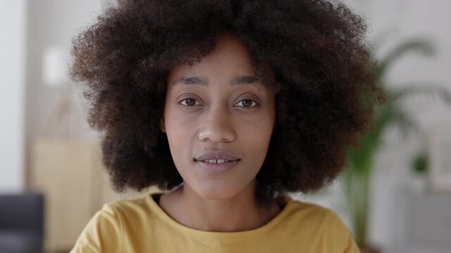 Headshot portrait of a confident young black woman with a curly afro hairstyle looking directly at the camera with a gentle and warm smile, showcasing her natural beauty and positive attitude