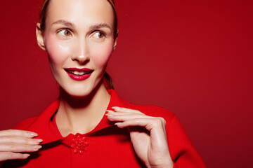 Young woman with red lipstick and red sweater looks aside with smile on red background. Close-up...