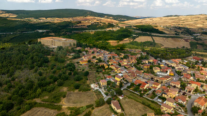 Panorama of Lagopesole, a town in Basilicata, Italy. Aerial view of a picturesque hillside village nestled among lush green forests and rolling fields, featuring a prominent castle on the crest.