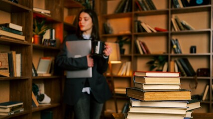 Young woman holding a laptop and mug in a library with bookshelves filled with books © shine.graphics