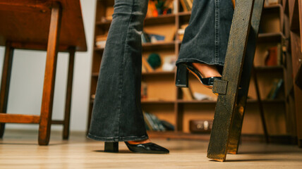Woman in flared jeans and heels climbing a wooden ladder in a library setting © shine.graphics