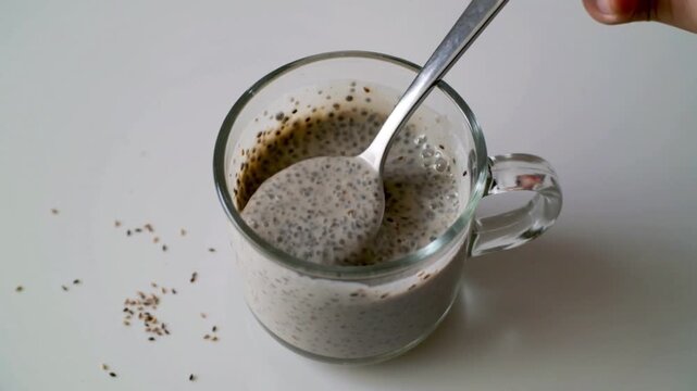 Cup filled with chia seeds being stirred with a spoon on a white surface featuring stirring, breakfast, healthy