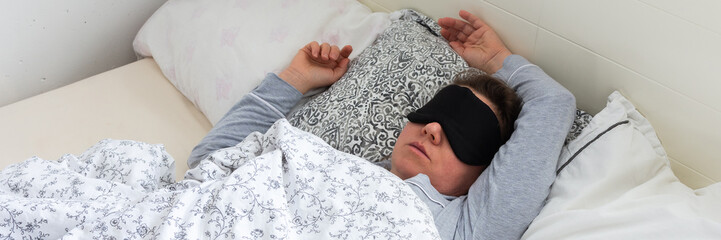A 50-year-old woman is sound asleep in her bed, wearing a sleep mask. She is surrounded by pillows...