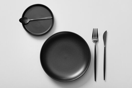 Table setting with black cutlery and plates on grey background
