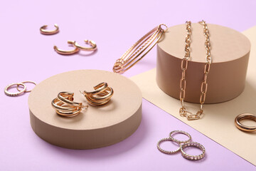 Beautiful golden necklace, bracelet, rings and earrings with podiums on color background