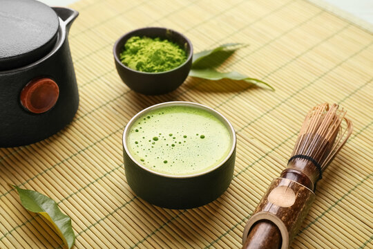 Bamboo mat with cup of fresh matcha tea, powder, chasen and teapot, closeup