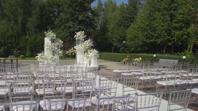 Empty chairs ready. Anticipation builds for outdoor gathering. Seats arranged for ceremony under towering leafy canopies. Event staging with vacant seats and floral centerpiece in tranquil setting