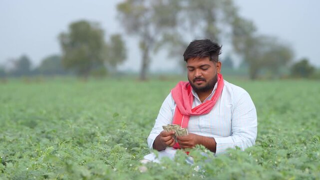 Young indian farmer counting money at agriculture field
