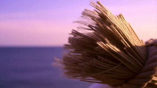 Close-up view of a thick rope with frayed ends against a serene ocean background during sunset, featuring soft purple hues in the sky
