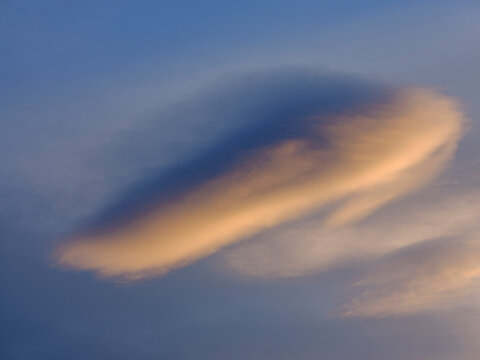 A lenticular cloud glows with sunset colors against a blue sky. Adamello Brenta Natural Park,Madonna di Campiglio,Trentino,Italy