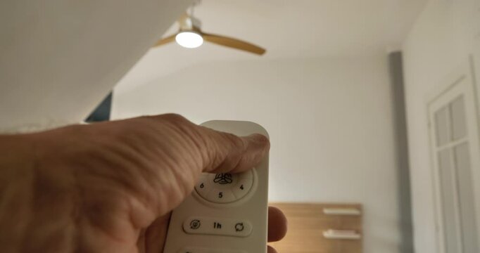 Ceiling Fan Control: A hand aims and presses the buttons on the remote control, activating the overhead fan.