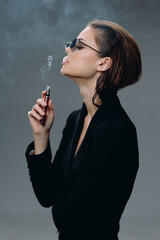 Fototapeta premium stylish woman smoking vape with sunglasses in black outfit, modern, confident, smoke, minimalistic