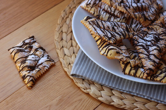 Italian sweet crisp pastry deep-fried and sprinkled with dark chocolate on wooden table. Chiacchere or crostoli, bugie, cenci 