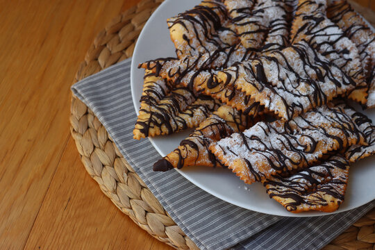 Italian sweet crisp pastry deep-fried and sprinkled with dark chocolate on wooden table. Chiacchere or crostoli, bugie, cenci 