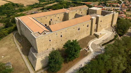 Aerial closeup of Lagopesole Castle, located in Basilicata, Italy. It is a medieval fortification dating back to the time of Frederick II. The medieval fortress is surrounded by dense green forest.