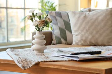 Vase with flowers and newspapers on table in interior of living room, closeup