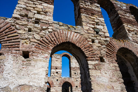 A layered perspective of the Church of Saint Sophia ruins in Nesebar, Bulgaria, showcasing the overlapping Byzantine stone and brick arches against a deep blue sky.