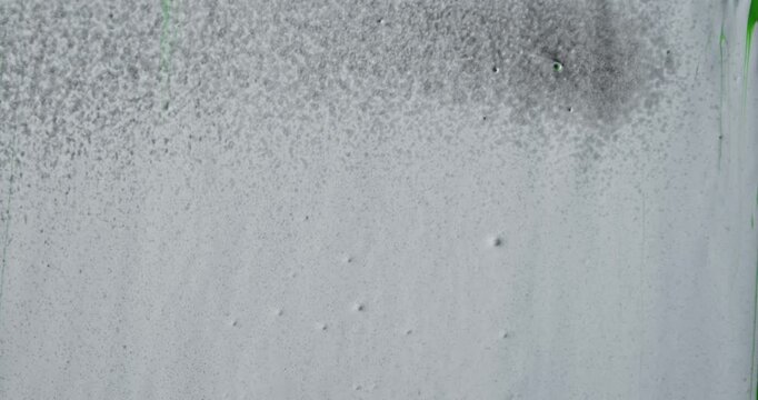 Close up of an abstract texture of white paint onto which water is sprayed, causing the paint to run down the glass vertical surface in tiny droplets. For design, grunge layouts, or advertisements.