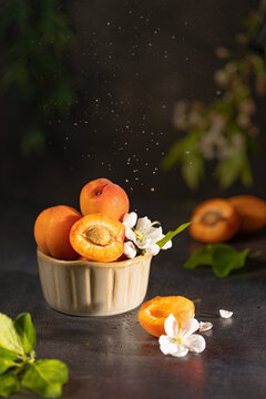 Fresh apricots in a bowl with delicate white blossoms and falling water splashes, symbolizing freshness and healthy summer eating