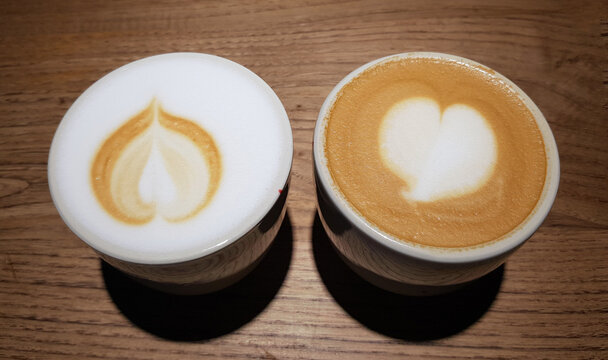 Two cups of coffee with heart designs sit on a wooden table duri