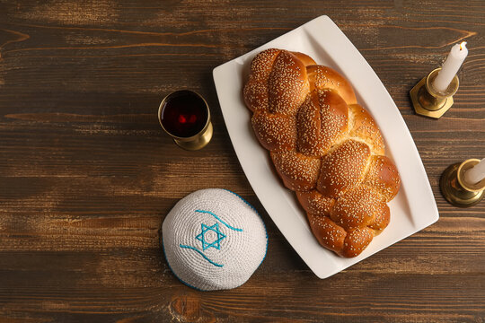 Traditional challah bread with wine goblet, kipa and burning candles on wooden table. Shabbat Shalom