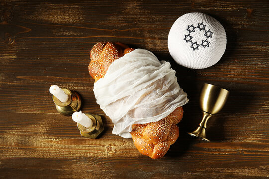Traditional challah bread with wine goblet, kipa and burning candles on wooden table. Shabbat Shalom