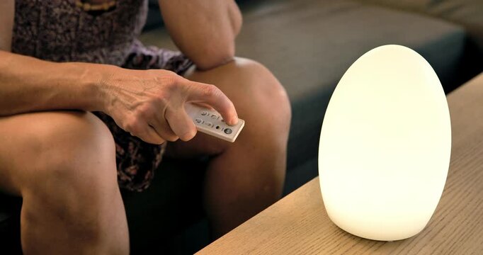 Illuminated Serenity: An individual holds a remote control near a glowing egg-shaped lamp, which casts a warm ambiance. A depiction of the convergence of technology and tranquility