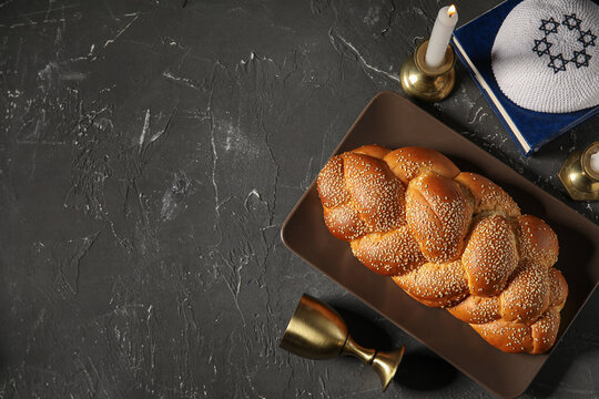 Traditional challah bread with wine goblet, kipa and burning candles on grey grunge table. Shabbat Shalom