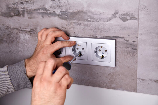  An electrician installs an electrical outlet using a screwdriver on a wall covered with porcelain tiles