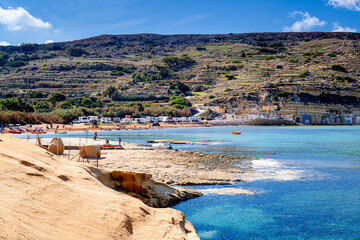 Fototapeta premium Tourists on picturesque beach on coast Malta on sunny day, Gnejna Bay, Għajn Tuffieħa.