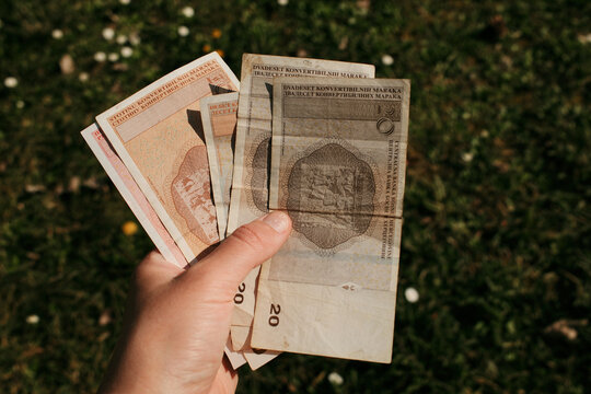Hand holding Bosnia and Herzegovina convertible mark banknotes outdoors on grass background. Financial concept of cash payment, currency exchange, and personal finance.