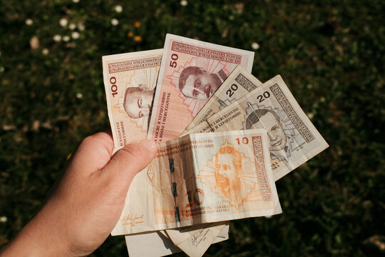 Hand holding Bosnia and Herzegovina convertible mark banknotes with grass background. Cash currency used for payments and financial transactions in Bosnia and Herzegovina.