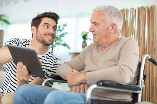 cheerful disabled retired man sitting in wheelchair near bearded son