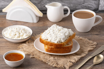 Fototapeta premium Breakfast setup with bread, cottage cheese, coffee, and jam on a wooden table in a cozy kitchen setting