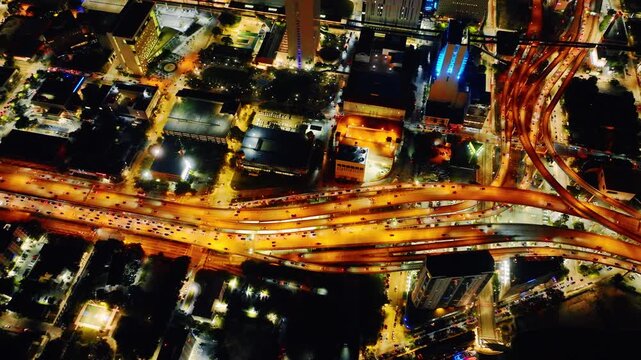 Perspective of a multi-level city road junction with glowing car lights and urban blocks. Top down aerial view of complex highway interchange at night. Miami downtown.